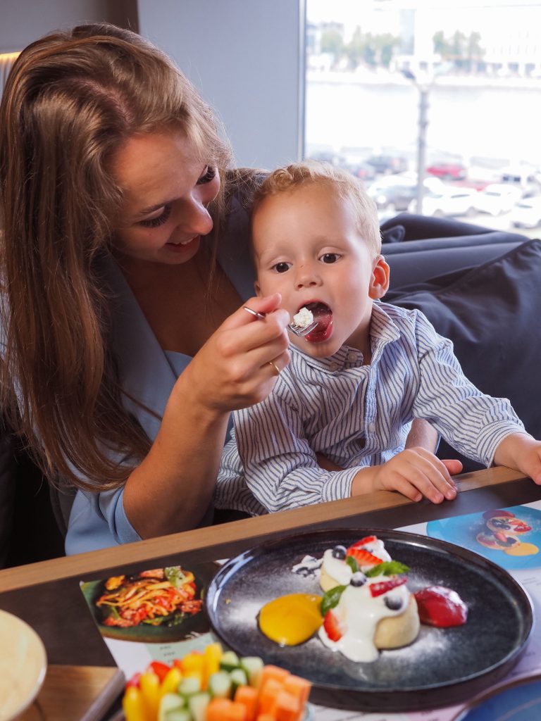 Mother lovingly feeds her child dessert, creating a warm family moment in a cozy cafe environment.